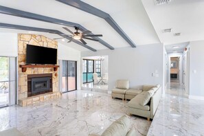 A spacious living area with a stone fireplace, a ceiling fan, and a large flat-screen TV mounted on the wall. - Hernando Beach 3BR - Water Views, Fireplace (Hernando Beach)