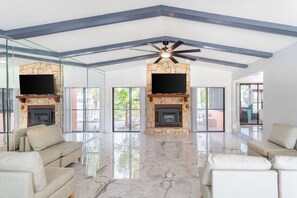 A spacious living room with a high ceiling, stone fireplace, flat-screen TVs, and a marble floor. - Hernando Beach 3BR - Water Views, Fireplace (Hernando Beach)