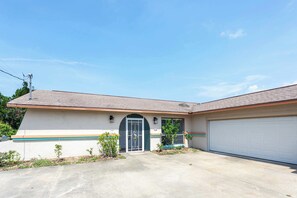 A single-story house with a garage, a front door with a decorative glass panel, and a small front yard with young trees. - Hernando Beach 3BR - Water Views, Fireplace (Hernando Beach)