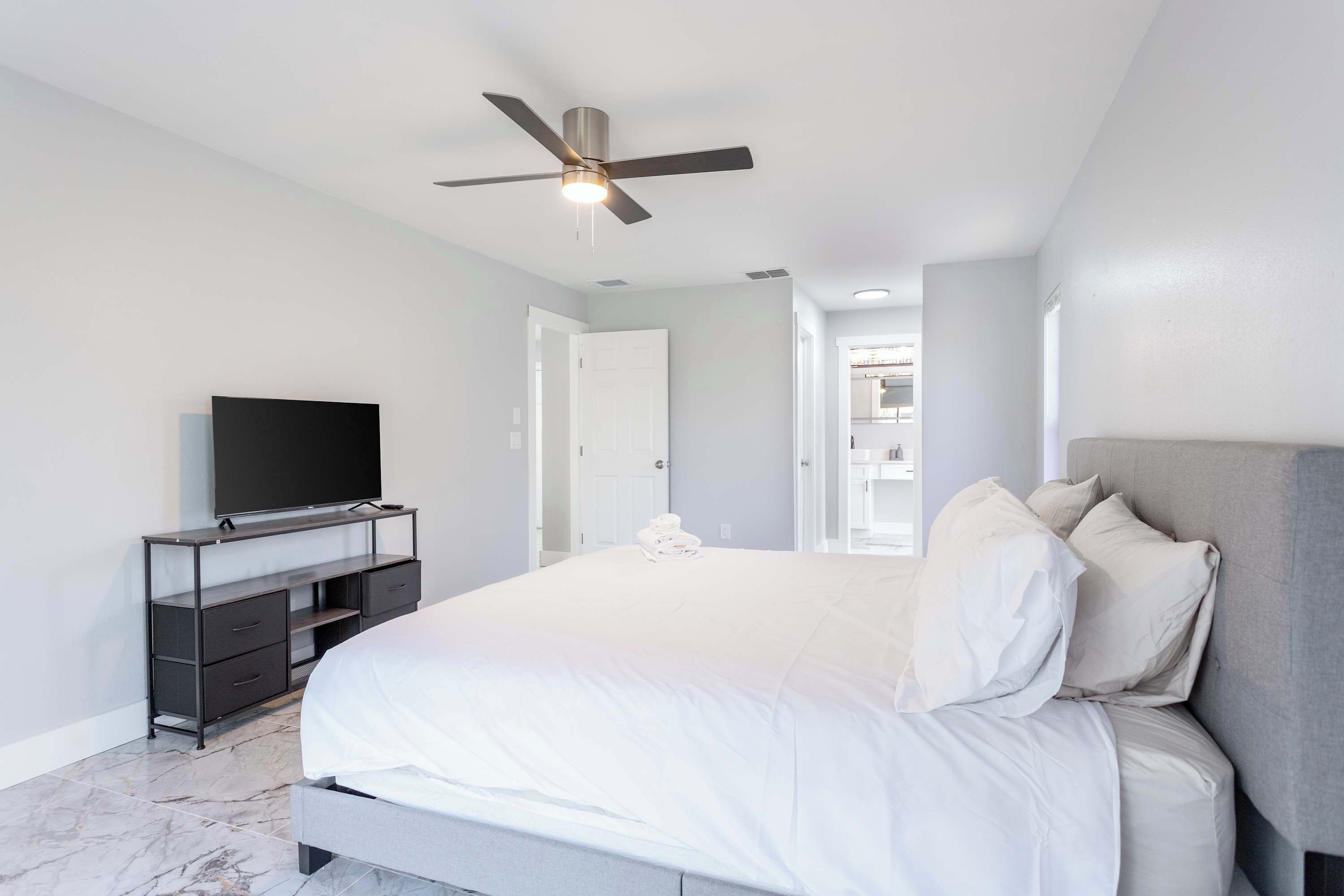 A modern bedroom with a bed, a television on a stand, and a ceiling fan.