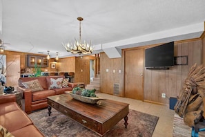 A living room with a brown leather sofa, a wooden coffee table, and a chandelier. - Lakeside Walk-In from House - Luxury Lake Cabin - Big Views - Pool Table (Shell Knob)
