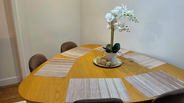 A round wooden table with a potted orchid, a decorative plate, and a placemat with text. - Place du Trocadéro (5-minute walk) - Elegant 3-room apartment, 50 m² (max. 6 people) (Paris)