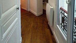 A corridor with wooden flooring, white walls, and a door leading to a room with a radiator and a window with a metal railing. - Place du Trocadéro (5-minute walk) - Elegant 3-room apartment, 50 m² (max. 6 people) (Paris)