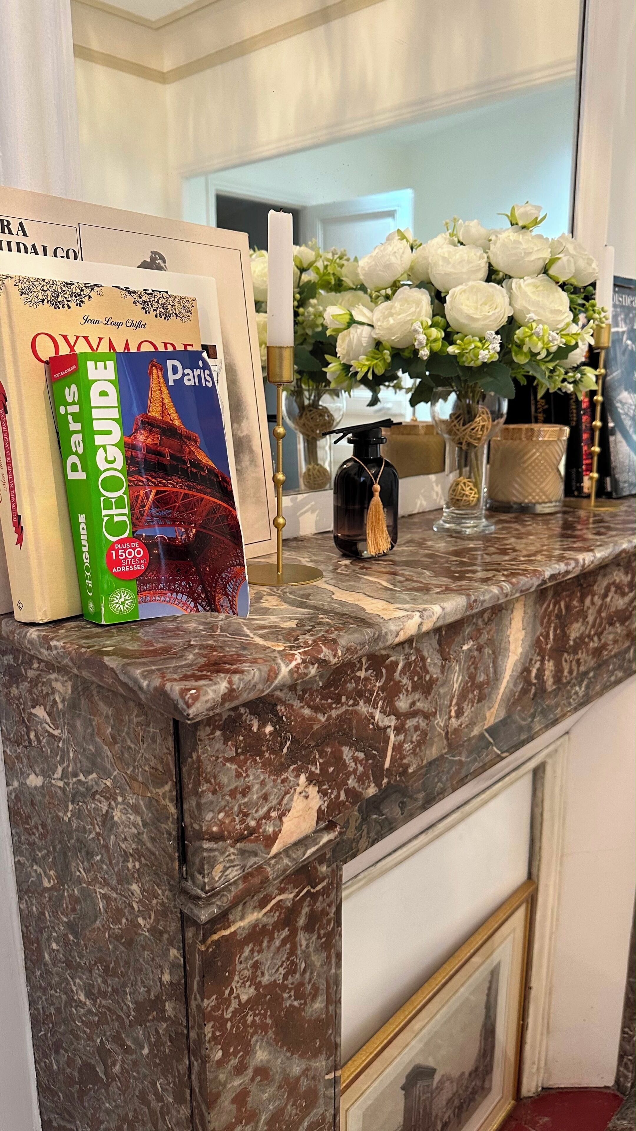 Eine Marmorarbeitsplatte mit einem Exemplar des Paris-Reiseführers, einer Vase mit weißen Blumen und einem Kerzenhalter.