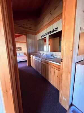 Interieur van een houten hutje met een badkamer, voorzien van een wastafel, spiegel en handdoekhouder.
