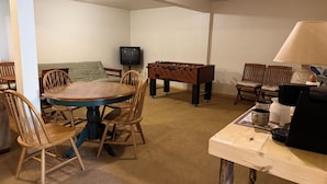 A room with a round wooden table, chairs, a foosball table, a television, and a coffee maker. - Rio Grande River and Ridge Lodge (South Fork)