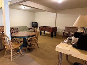 Ein Zimmer mit einem runden Holztisch, Stühlen, einem Kicker, einem Fernseher und einer Kaffeemaschine.