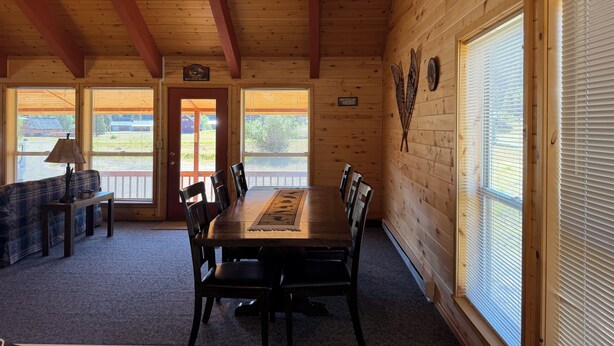 A wooden interior with a dining table, chairs, a lamp, and large windows. - Rio Grande River and Ridge Lodge (South Fork)