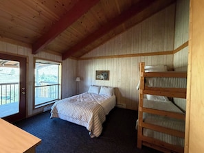 A wooden cabin room with a bunk bed, a bed with a quilt, a desk, and a window with a view of the outdoors. - Rio Grande River and Ridge Lodge (South Fork)