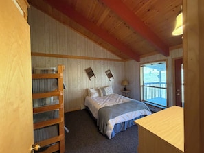 Ein Schlafzimmer mit Etagenbett, einem Bett mit grauer und weißer Bettdecke, einem Nachttisch mit Lampe und einem Fenster mit Blick ins Freie.