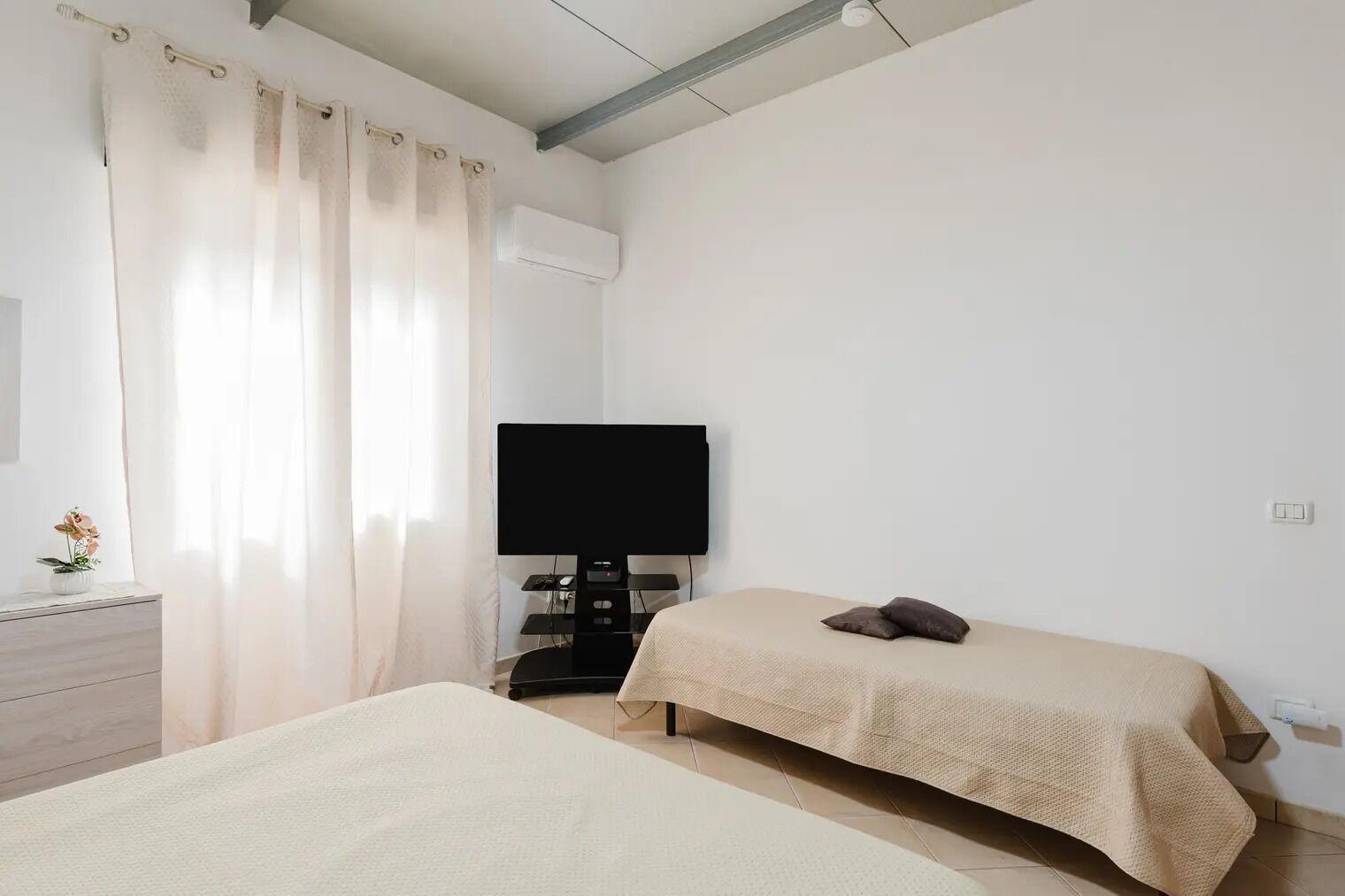 A bedroom with a bed, a TV on a stand, a dresser, and a window with curtains.