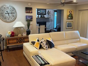 Een woonkamer met een bank, een klok, een lamp en diverse decoraties aan de muur.