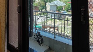Vista desde una habitación con puerta que da a un balcón. El balcón tiene barandilla metálica y vistas a un paisaje montañoso bajo un cielo despejado.