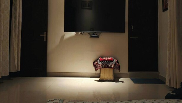 Una habitación con ventilador de techo, televisor de pantalla plana montado en la pared, alfombra estampada en el suelo y una puerta con cortina.