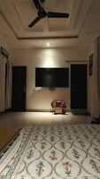 Una habitación con ventilador de techo, televisor de pantalla plana montado en la pared, alfombra estampada en el suelo y una puerta con cortina.