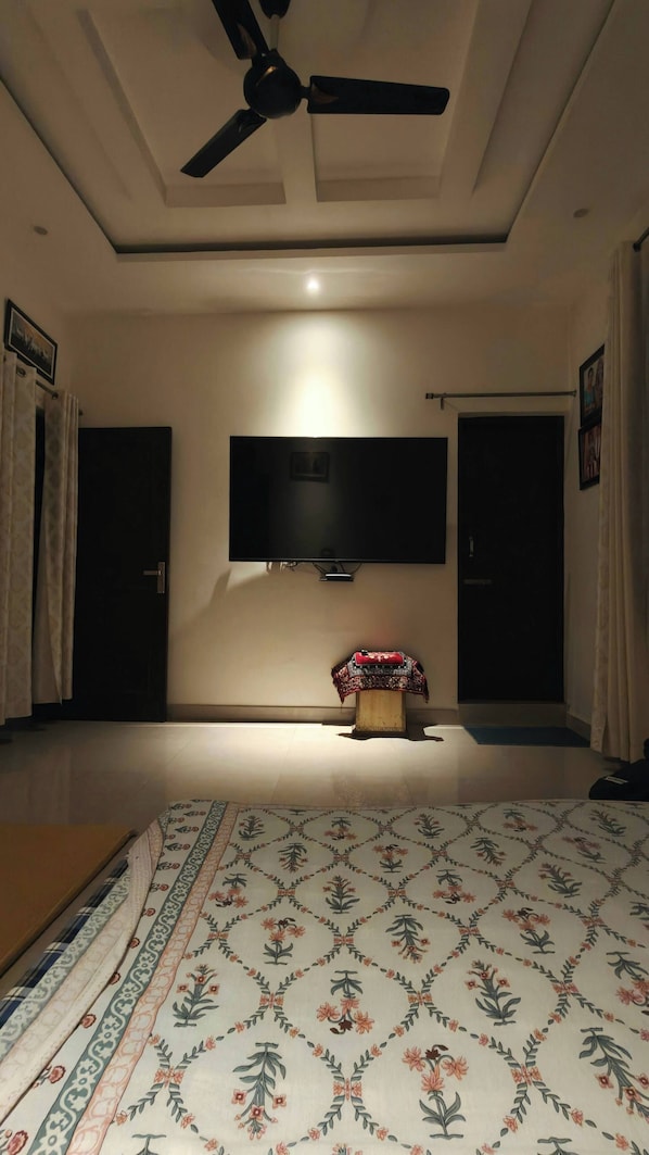 A room with a ceiling fan, a flat-screen TV mounted on the wall, a patterned rug on the floor, and a door with a curtain.