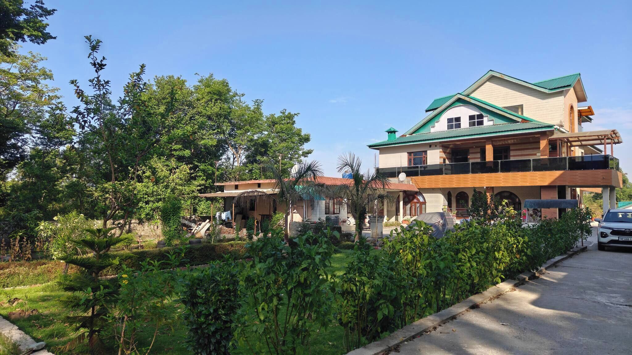 A two-story building with a balcony, surrounded by lush greenery and a clear sky.