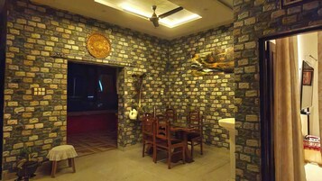 Quarto com parede de pedra, ventoinha no teto, mesa de jantar com cadeiras e uma pequena mesa com toalha branca.