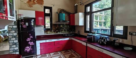 Una cocina con armarios rojos, un refrigerador negro, una ventana con vistas y un piso con diseño.