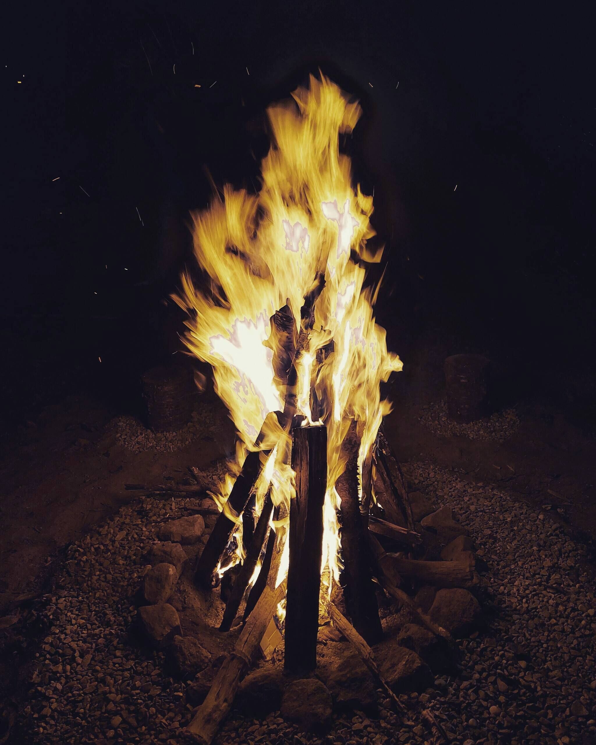 Un feu de camp avec des bûches disposées en forme de tipi, entouré de rochers.