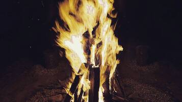Un feu de camp avec des bûches disposées en forme de tipi, entouré de rochers.