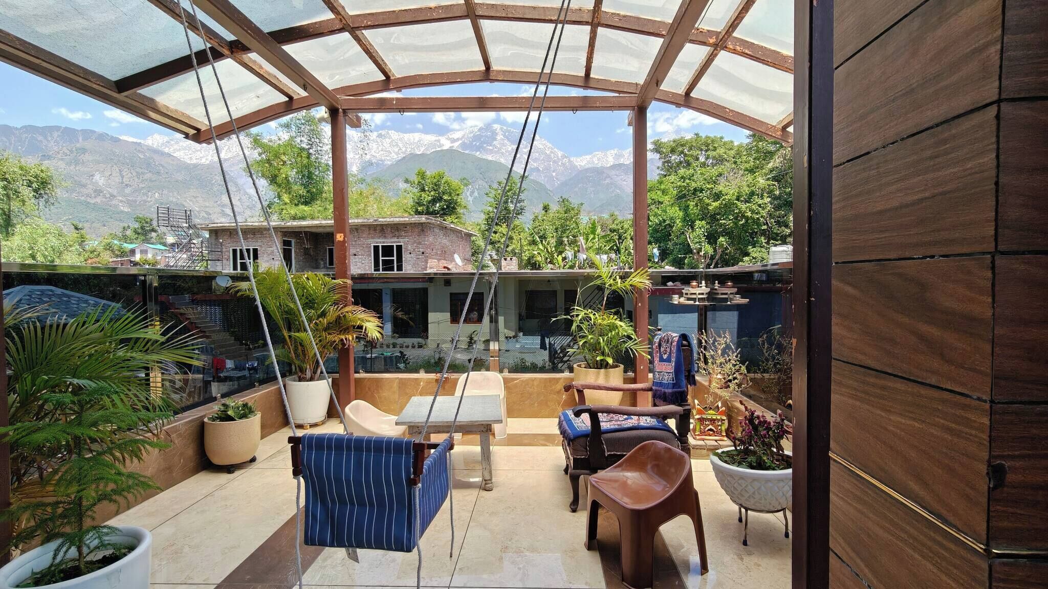 A covered patio with a view of a mountain range, outdoor furniture, and potted plants.