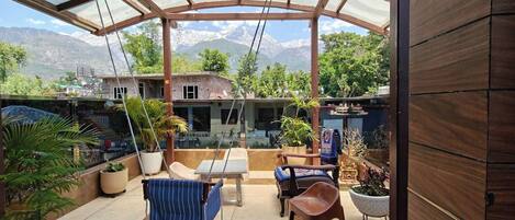 A covered patio with a view of a mountain range, outdoor furniture, and potted plants.