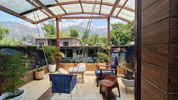 A covered patio with a view of a mountain range, outdoor furniture, and potted plants.