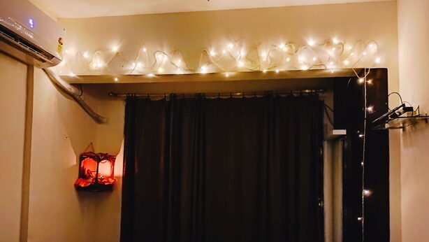 Ein Zimmer mit einem Bett, einer Wand-Klimaanlage, einem Vorhang und einer Wandleuchte.