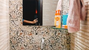 Ein Badezimmer mit einem weißen Waschbecken, einem Spiegel und Wandverkleidung mit Muster.
