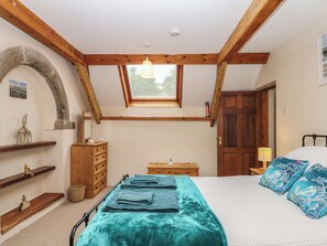 A bedroom with a sloped ceiling, a bed with blue and white bedding, a wooden dresser, a nightstand, a window, and a door. - Brimble Cottage at Dockwell Farm (Newton Abbot)