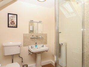 Un baño con inodoro, lavamanos, espejo y cabina de ducha de vidrio.