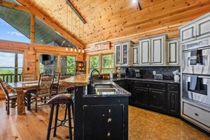 A wooden cabin interior with a kitchen, dining area, and a bar. - Luxury Log Cabin | Epic Views, Hot Tub, Sleeps 12 (Mineral Bluff)