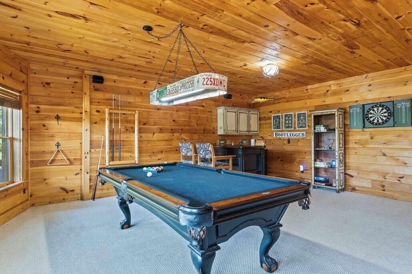 A wooden interior with a pool table, billiard cues, and a dartboard.