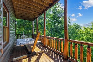 A wooden deck with a hammock and a wooden railing. - Luxury Log Cabin | Epic Views, Hot Tub, Sleeps 12 (Mineral Bluff)