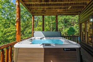 A hot tub on a wooden deck with a view of a forest.