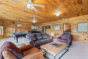 A wooden cabin interior with a pool table, sofas, a coffee table, and a ceiling fan. - Luxury Log Cabin | Epic Views, Hot Tub, Sleeps 12 (Mineral Bluff)