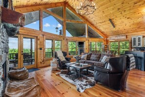 A spacious cabin with a high ceiling, large windows, a fireplace, and a cozy seating area. - Luxury Log Cabin | Epic Views, Hot Tub, Sleeps 12 (Mineral Bluff)