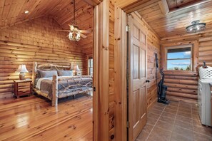 A log cabin interior with a bed, a ceiling fan, a window, and a vacuum cleaner.