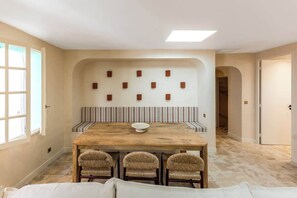 Ein Essbereich mit einem Holztisch, drei Stühlen, einer Bank und einer Wandleuchte.
