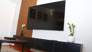 A flat-screen TV mounted on a wall above a black cabinet with a potted plant beside it.