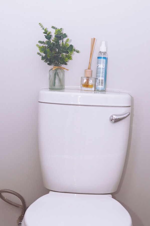A toilet with a white tank and seat, a small potted plant, and a bottle of liquid on top.