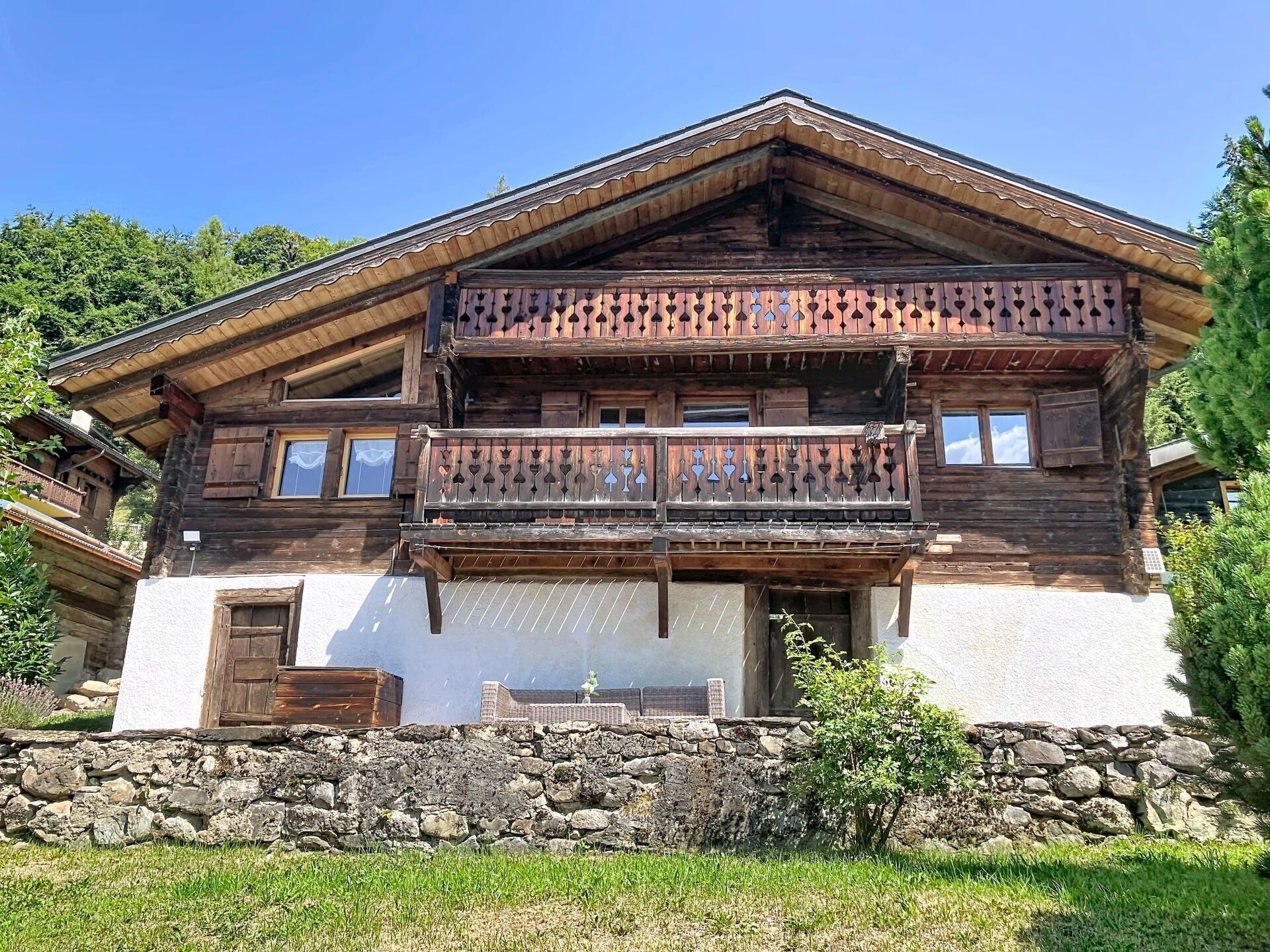Ein traditionelles Holzhäuschen mit Steinunterbau, einem Balkon mit dekorativer Geländer und einer weißen Außenwand.