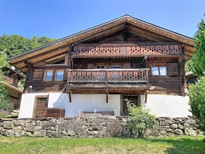 Ein traditionelles Holzhäuschen mit Steinunterbau, einem Balkon mit dekorativer Geländer und einer weißen Außenwand.