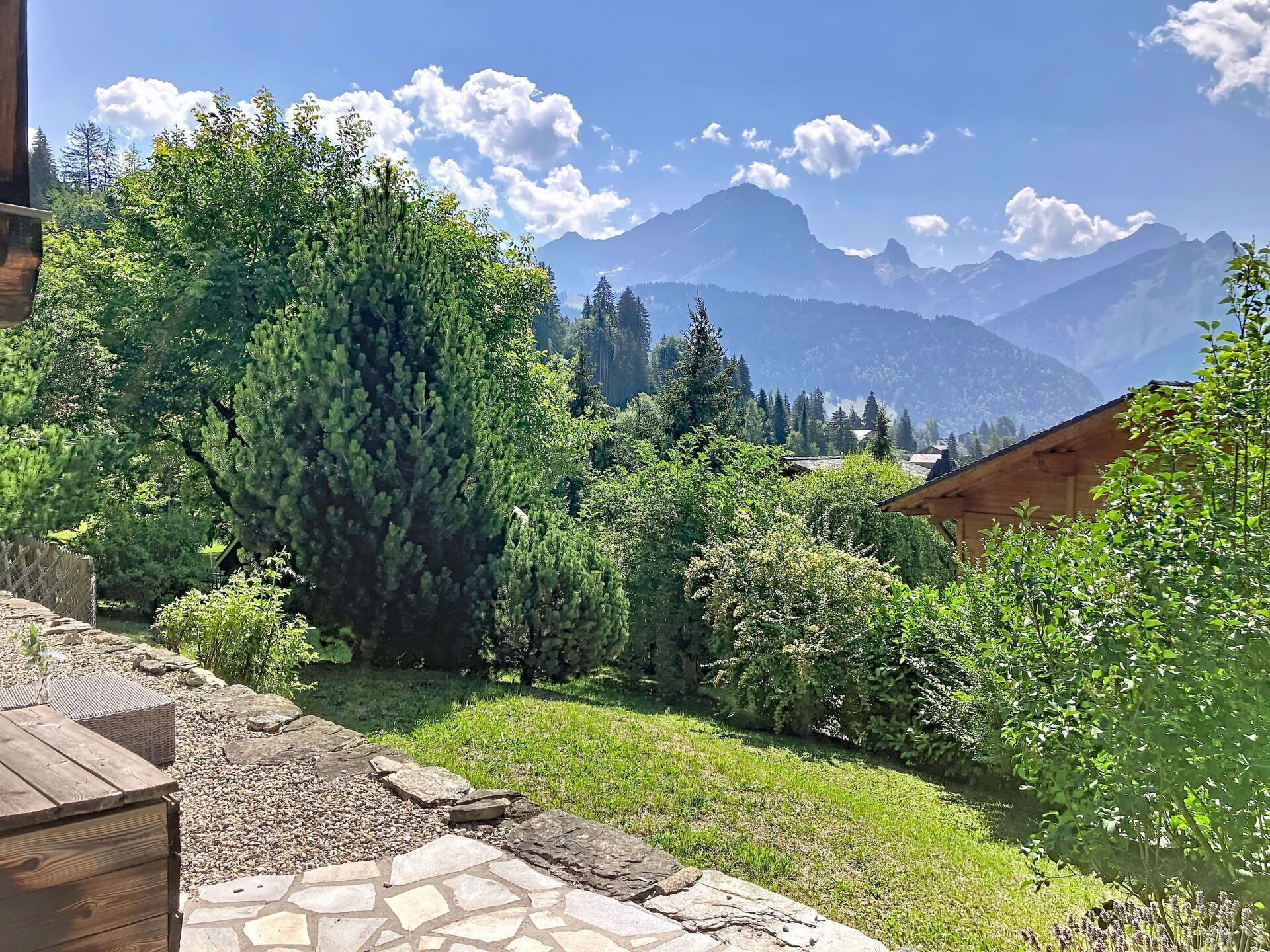 Ein Garten mit einem gepflasterten Weg, üppigem Grün und einer Bergsicht im Hintergrund.