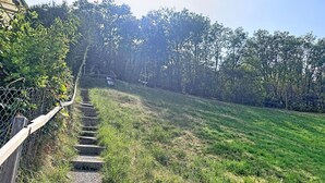 Una escalera de madera que sube por una pendiente cubierta de césped, rodeada por una cerca de malla y árboles frondosos.