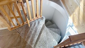 Una escalera de madera conduce a una habitación pequeña y circular con piso de baldosas.