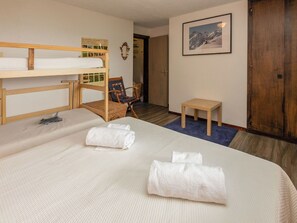 Ett hotellrum med en våningssäng, ett litet träbord, en stol, en inramad tavla på väggen och en dörr.