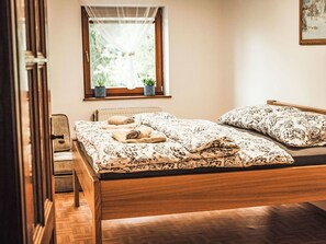 A bedroom with a wooden bed, two pillows, a window with plants, and a radiator.