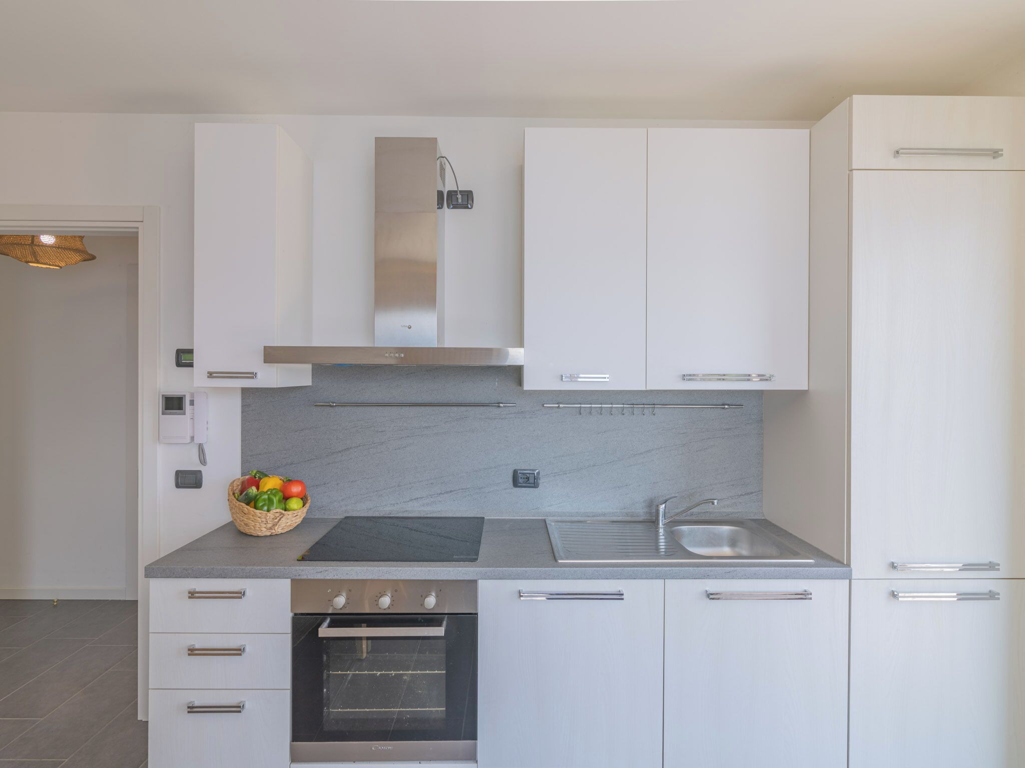 A modern kitchen with white cabinetry, a stainless steel range hood, a built-in oven, and a granite countertop.